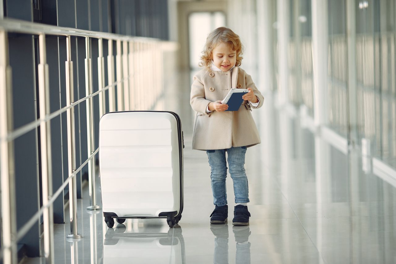 공항 복도에서 작은 여행가방 옆에 서 있는 어린이